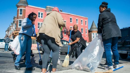 Volunteers clean up rubbish and shattered glass in front of a looted business in Baltimore. (AAP)