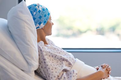 Young woman in bed suffering from cancer. Thoughtful woman battling with tumor looking out of window. Young patient with blue headscarf recovery in hospital on bed.