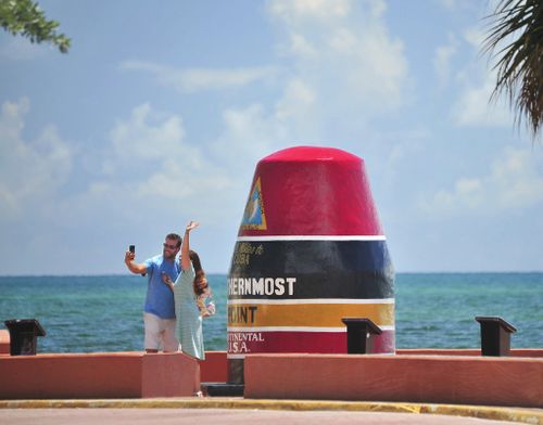 Key Westers James Sandlin, left, and Chloe Hodgdon, take advantage of a deserted "Southernmost Point of the United States" park to take a photo while waving to relatives via a nearby webcam. (AP)