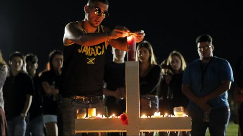 Joey Kandil, 18, a recent graduate of Marjory Stoneman Douglas High School, places a ring around a candle on one of seventeen crosses, after a candlelight vigil for the victims of the Wednesday shooting at the school. (AAP)