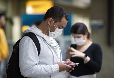 Passengers wearing masks as a precaution against the spread of the new coronavirus COVID-19 use their phones at the Sao Paulo International Airport in Sao Paulo, Brazil, Thursday, Feb. 27, 2020. (AP Photo/Andre Penner)