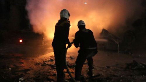 This photo provided on Sunday, Jan. 7, 2018 by the Syrian Civil Defense White Helmets, which has been authenticated based on its contents and other AP reporting, shows Syrian White Helmet civil defense workers extinguishing fire following a bombing that targeted the office of Ajnad al-Koukaz, a militant group consisting of foreign fighters mostly from the Caucuses and Russia, in Idlib, Syria. A Syrian monitoring group and paramedics in northwestern Syria say the death toll from a massive bombing has risen to at least 25 in addition to nearly 100 others wounded. (Syrian Civil Defense White Helmets via AP)