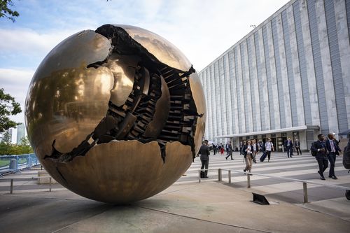 People walk around the plaza by the Sphere Within Sphere outside the United Nations Headquarters.