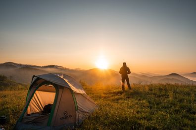 Man standing out watching the sunrise with his tent pitched in the foreground