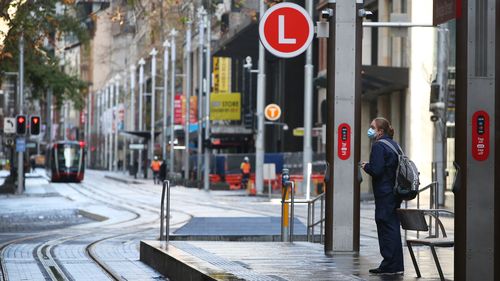 A frontline worker awaits the a tram on George Street in Sydney amid the city-wide lockdown. Sydney lockdown