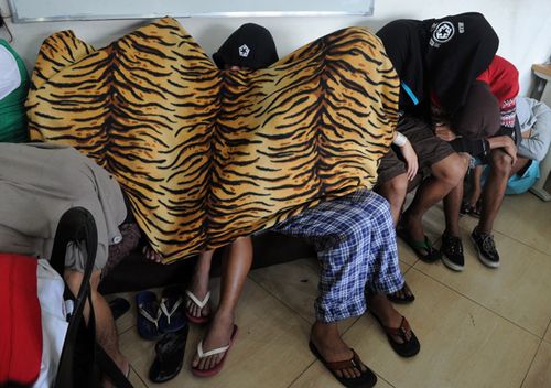 Suspects in an alleged Internet porn operation cover themselves at the Cybercrime Division of the NBI in Manila on Fenruary 18, 2014.