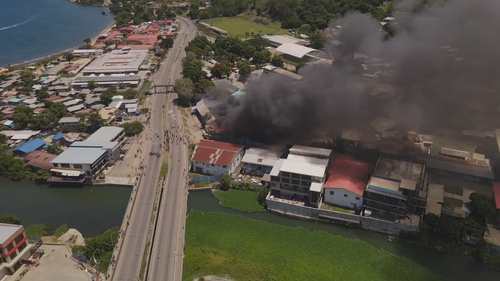 Thick smoke billows across properties in the Solomon Islands city as crowds fill the streets.