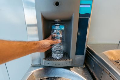 Young man refilling his plastic water bottle at the airport. His POV.