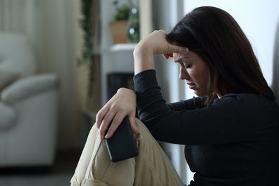 Sad woman holding smart phone complaining at home