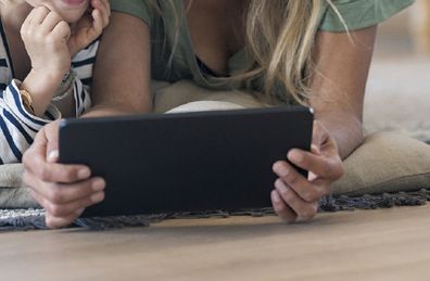 Babysitter reading texts with child on floor.