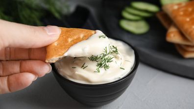 Woman dipping cracker into tasty creamy dill sauce at grey table, closeup