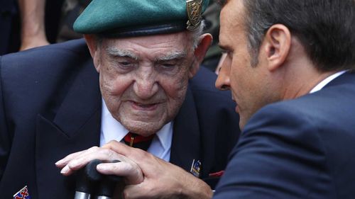 French President Emmanuel Macron holds the hand of French war veteran Leon Gautier, a member of the Kieffer commando.