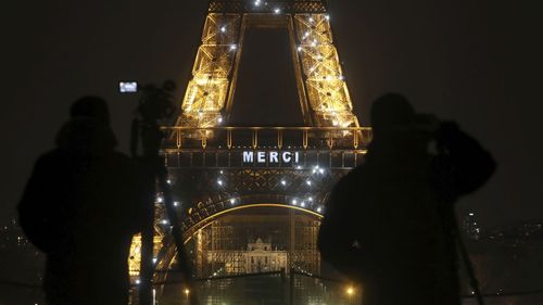 Cameramen stand in front of the Eiffel Tower where the word "Merci", the French word for 'Thank you", is emblazoned as France's coronavirus death toll continued to climb, in Paris, Friday, March 27, 2020