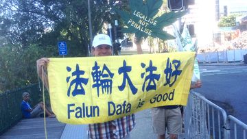 Falun Dafa and Legalise Marijuana protesters hold up signs to Tony Abbott's motorcade. (9NEWS)