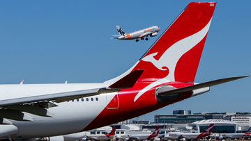 Qantas aircraft on tarmac and Jetstar plane flying in the background