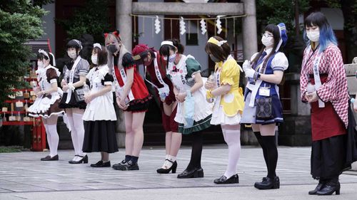Employees dressed in maid costumes from several maid-themed cafes of Akihabara line up at the precinct prior to a prayer-meeting for protection from COVID-19 in Tokyo.