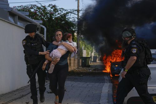 Police officers evacuate a woman and a child from a site hit by a rocket fired from the Gaza Strip, in Ashkelon, southern Israel, Saturday, Oct. 7, 2023.  