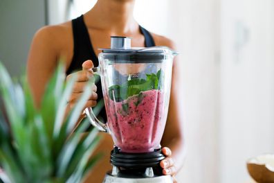 A woman blends spinach, blueberries, banana and almond milk to make a healthy green smoothie