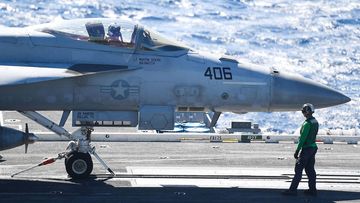 A green shirt &#x27;Hook Runner&#x27; crew member moves a Super Hornet into position prior to launching