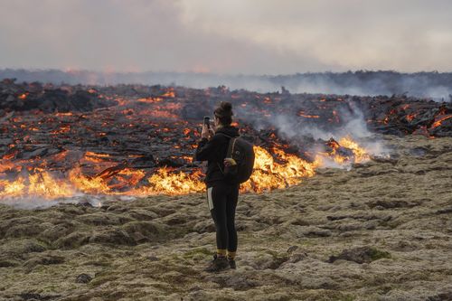 A person walks near lava emerging from a fissure of the Fagradalsfjall volcano near the Litli-Hrútur mountain, some 30 kilometres southwest of Reykjavik, Iceland, Monday July 10, 2023.  