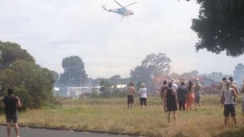 Hastings residents watch as a water-carrying helicopter dumps waters on a raging grass fire. (9NEWS)