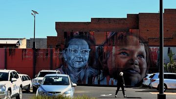 A woman walks across a car park in front of a mural on the side of a building on Talbragar Street in Dubbo, NSW. (Photo: Kate Geraghty)