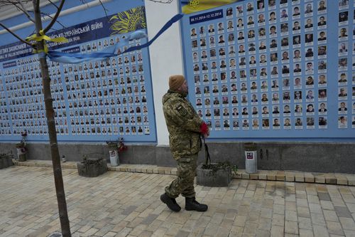 An Ukrainian serviceman holds a flower as he looks at the memorial wall outside of St. Michael's Golden-Domed Cathedral, in Kyiv, Ukraine, Friday, Feb. 24, 2023. 