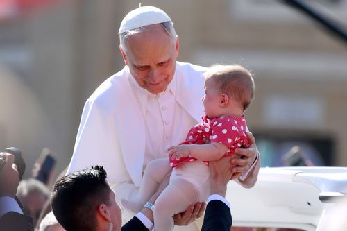 Pope Leo XIV holds a baby as he arrives ahead of the Inauguration Mass 