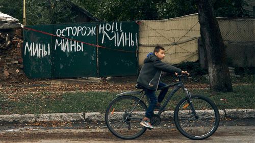 A teenager rides past a sign reading "Caution. Mines" in the liberated city of Izium in Ukraine.