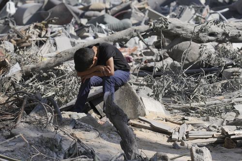 A Palestinian boy sits on the rubble of the building destroyed in an Israeli airstrike in Bureij refugee camp Gaza Strip, Wednesday, Oct. 18, 2023 
