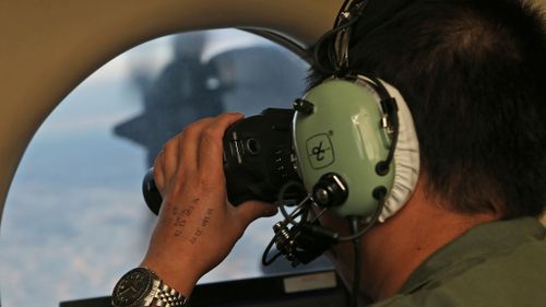  In this March 22, 2014, file photo, Flight Officer Jack Chen uses binoculars at an observers window on a Royal Australian Air Force P-3 Orion during the search for missing Malaysia Airlines Flight MH370. (AAP)