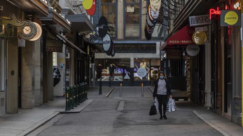 A lone shopper is seen carrying shopping bags as she walks down the usually busy Degraves Street laneway fame for its cafes and coffee as lockdown of Melbourne forces people to stay at home if not working due to the continuing spread of COVID-19. (Asanka Brendon Ratnayake)