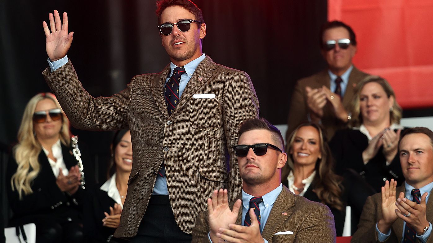 Brooks Koepka acknowledges the crowd at the Ryder Cup opening ceremony while a stony faced Bryson DeChambeau looks on.