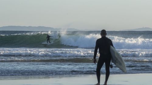 A man watches as another surfer rides a wave at The Pass in Byron Bay,close to the NSW, Queensland border, which is reopening on July 12.