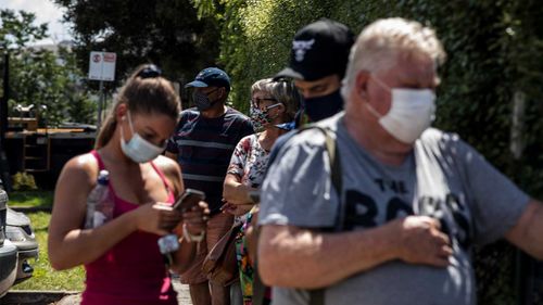 People wear face masks as they wait to receive a COVID-19 test outside the Sunbury Respiratory Clinic.