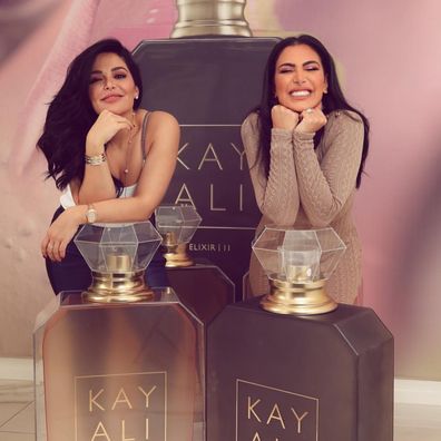 Mona Kattan (L) and sister Huda Kattan pose with giant Kayali bottles shortly after the brand launched in 2018.