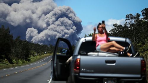 A woman takes a photo as an ash plume rises from the Kilauea volcano on Hawaii's Big Island on May 15, 2018.