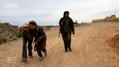 Tara Brown ducks for cover as she is guided along the front line by members of the YPJ.