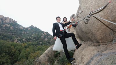 Adventurous newlyweds pose for wedding photos on cliff face