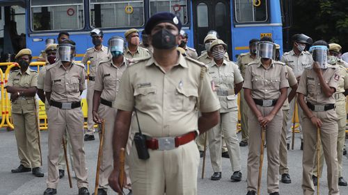 Indian police officials wearing face shields and masks as a precaution against the coronavirus stand guard during a protest against a pair of controversial agriculture bills in Bengaluru, India, Monday, Sept. 28, 2020. 