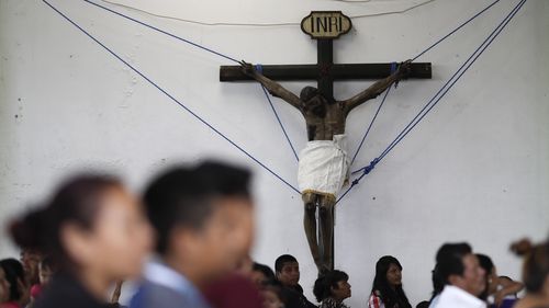 A crucifix, recovered from a collapsed church, is held up by ropes inside an auditorium during a Mass, in Tepeojuma. (AAP)