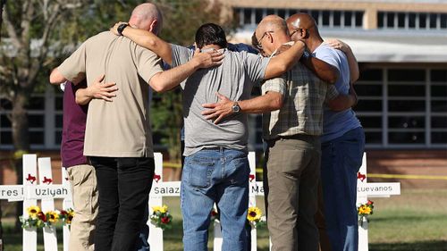 Мужчины образуют молитвенный круг на мемориале жертв стрельбы в начальной школе Робба в Овальди, штат Техас.