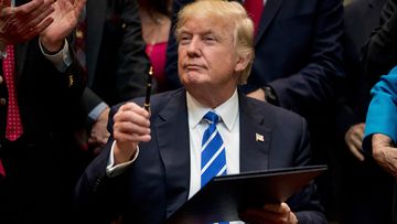 President Donald Trump holds up a pen he used to sign one of various bills in the Roosevelt Room of the White House in Washington. Ignoring fresh threats from the White House, city leaders across the U.S. are vowing to intensify their fight against Trump's promised crackdown on so-called "sanctuary cities" despite the financial risks. (AAP)
