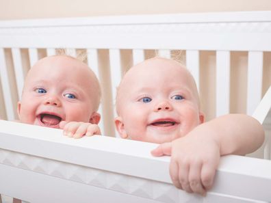 Twin baby boys peeking out of a bassinet.