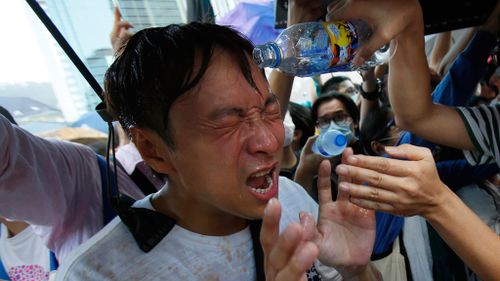 A student protester is overcome by pepper spray from riot police as thousands of protesters surround the government headquarters in Hong Kong. (AAP)