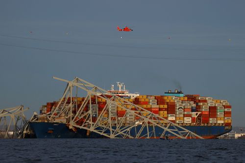 A helicopter flies over the Dali cargo vessel and the wreckage of the Francis Scott Key Bridge.