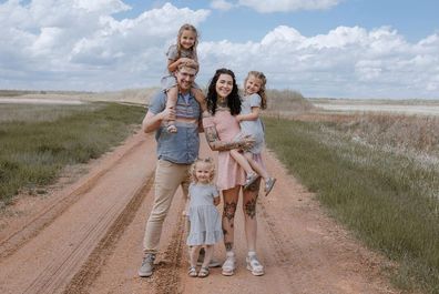 Family standing on orange dirt road, blue sky behind them. Cute family photo, all dressed tidy.