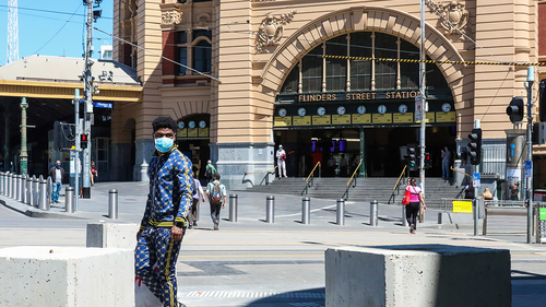 A man wearing a mask is seen walk past Flinders Street Station in Melbourne, Australia, Wednesday, Oct. 28, 2020. (AP Photo/Asanka Brendon Ratnayake)