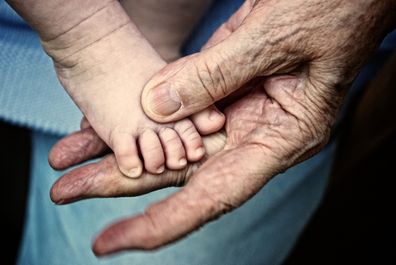Close up of senior woman's hand holding infant's foot, concept of time, aging, generations, affection, offspring