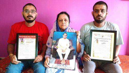 Anindita Mitra, 61, flanked by her sons Satyajit Mitra, right and Abhijit Mitra, pose with portraits of her husband late Narayan Mitra.